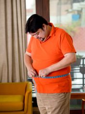 Overweight man measuring his waist size with tape measure